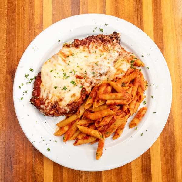 Chicken parmesan with melted cheese and penne pasta in red sauce on a white plate.