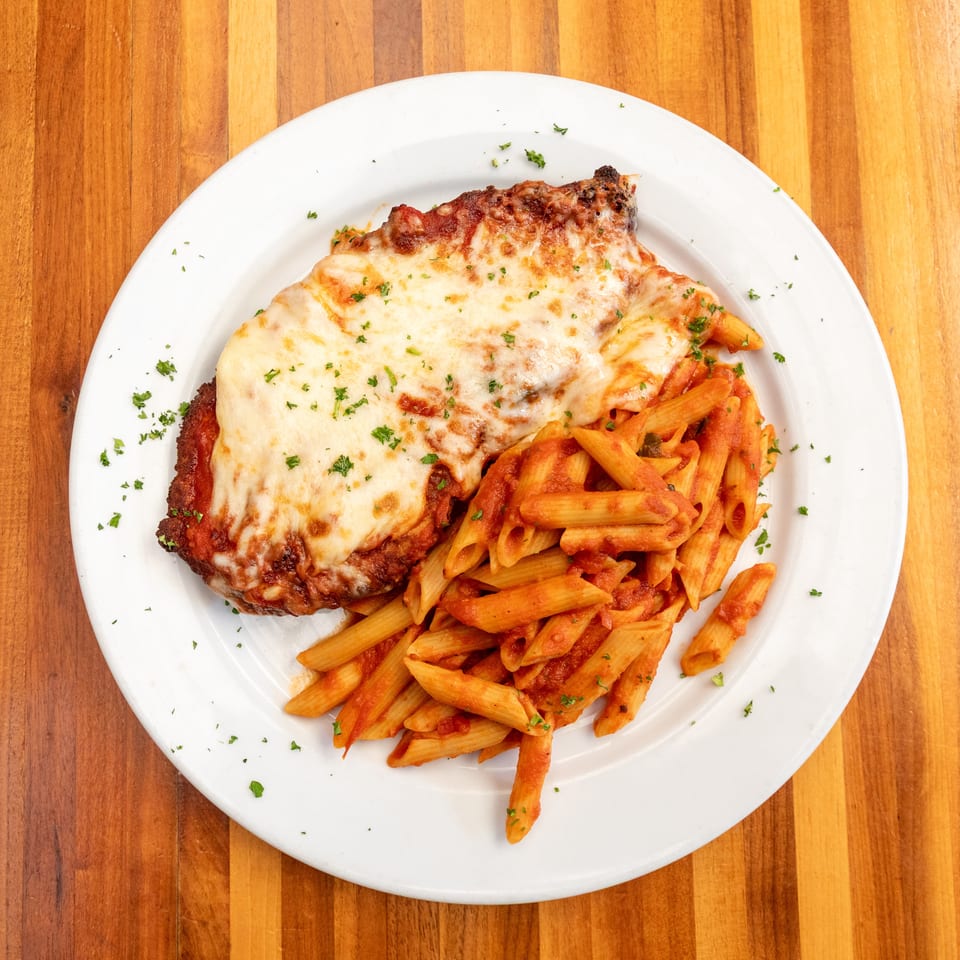 Chicken parmesan with melted cheese and penne pasta in red sauce on a white plate.