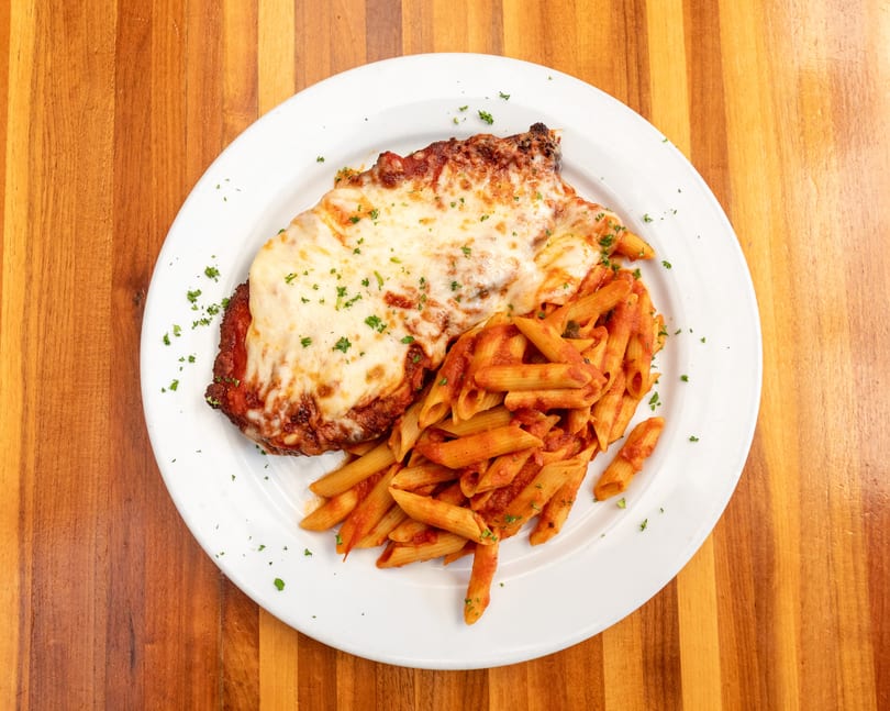 Chicken parmesan with melted cheese and penne pasta in red sauce on a white plate.