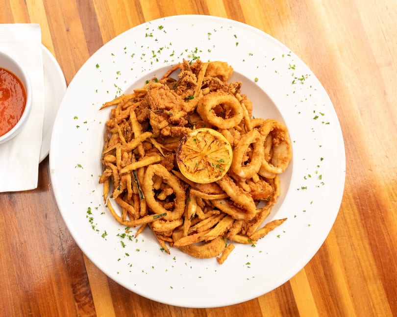 Crispy fried calamari and zucchini fries with a lemon slice and red sauce on a wooden table.