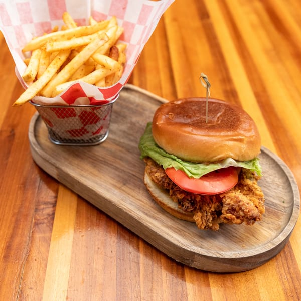 Crispy chicken sandwich with lettuce and tomato, served with a side of seasoned fries.