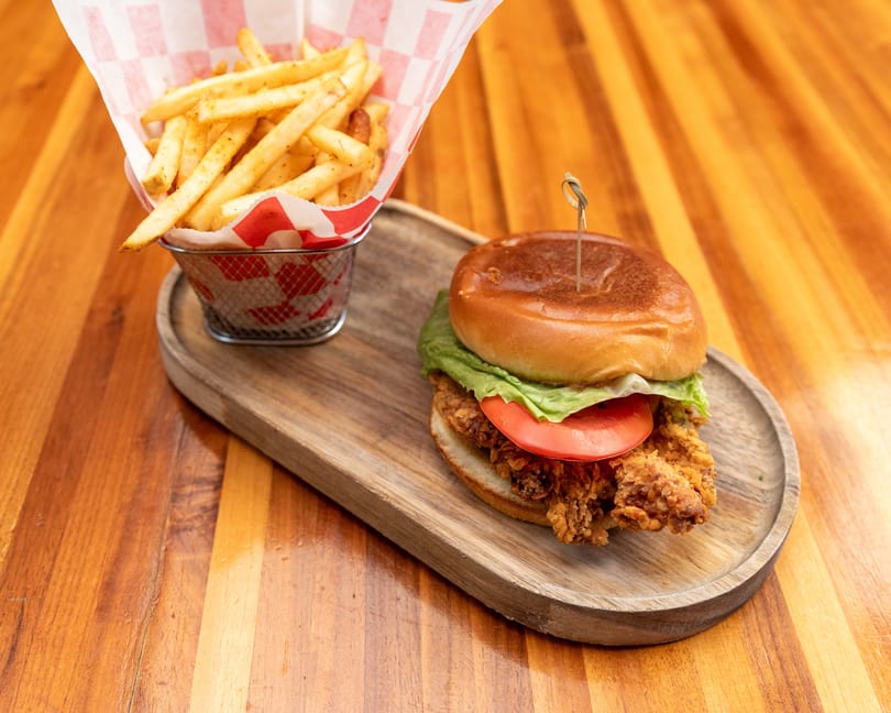 Crispy chicken sandwich with lettuce and tomato, served with a side of seasoned fries.