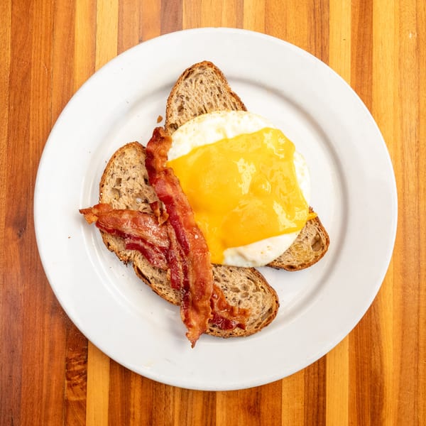 Breakfast plate with two slices of toast, a fried egg with melted cheese, and crispy bacon.