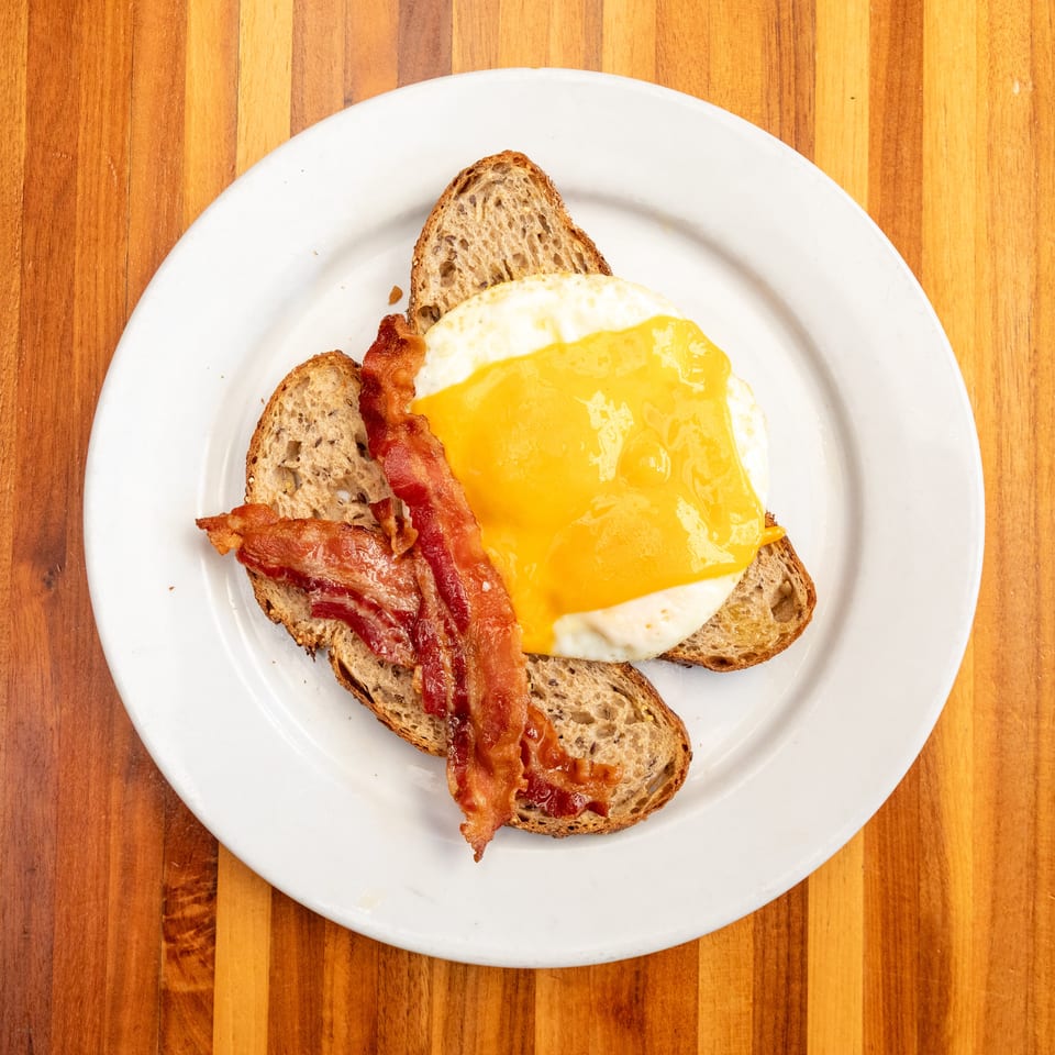Breakfast plate with two slices of toast, a fried egg with melted cheese, and crispy bacon.
