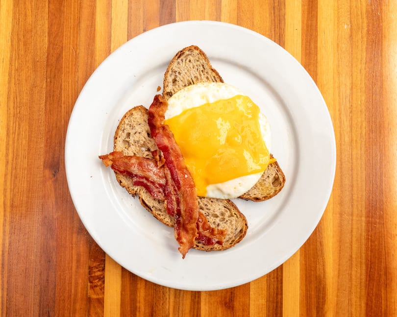 Breakfast plate with two slices of toast, a fried egg with melted cheese, and crispy bacon.