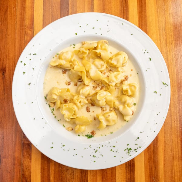 Tortellini pasta in a creamy sauce with chopped walnuts and parsley on a white plate.