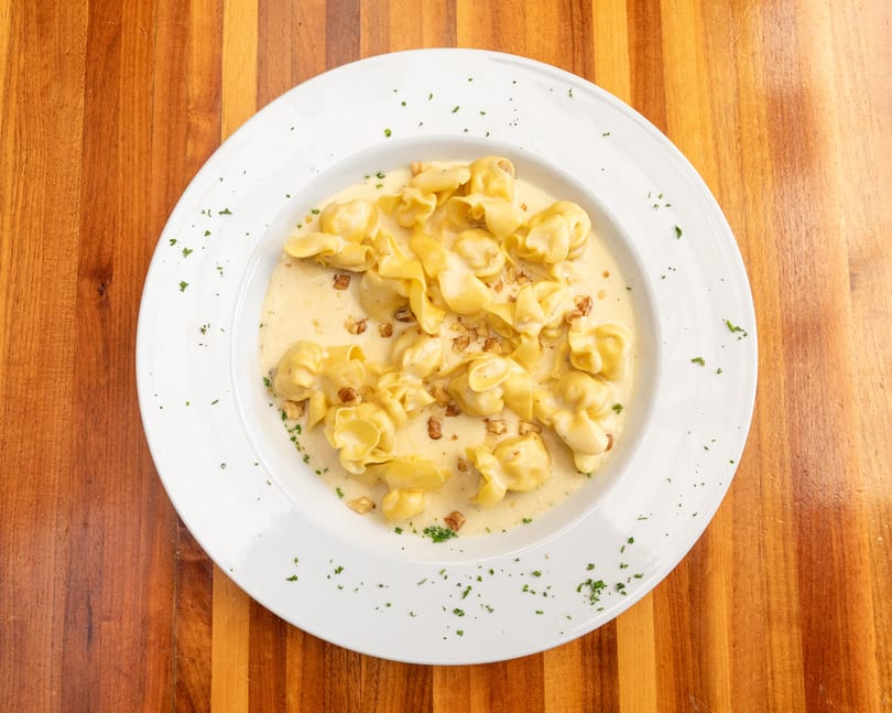 Tortellini pasta in a creamy sauce with chopped walnuts and parsley on a white plate.