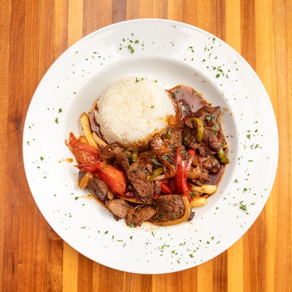 Lomo Saltado with steak, red and green peppers, onions, fries, and rice on a white plate.