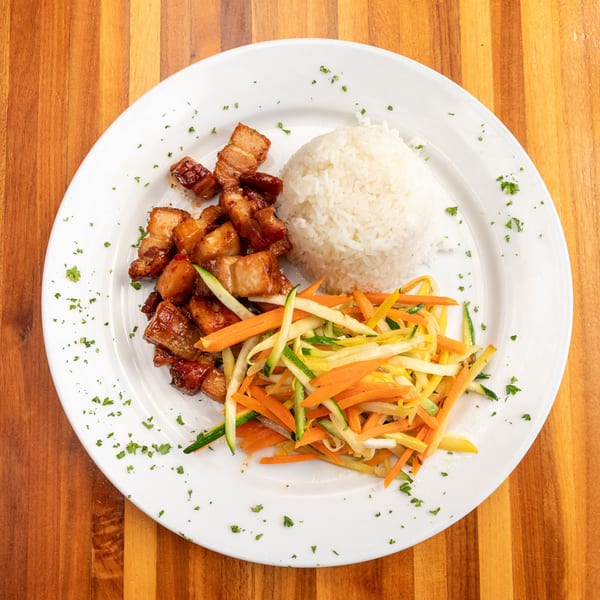Crispy pork belly with white rice and julienned carrots, zucchini, and yellow squash on a white plate.