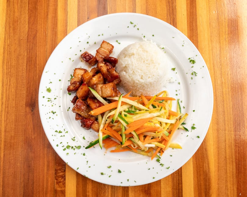 Crispy pork belly with white rice and julienned carrots, zucchini, and yellow squash on a white plate.