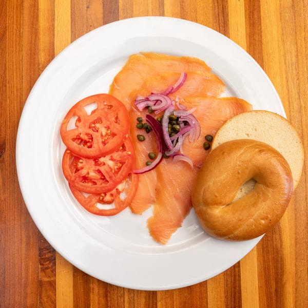 Smoked salmon with capers, red onions, tomato slices, and a bagel on a white plate.