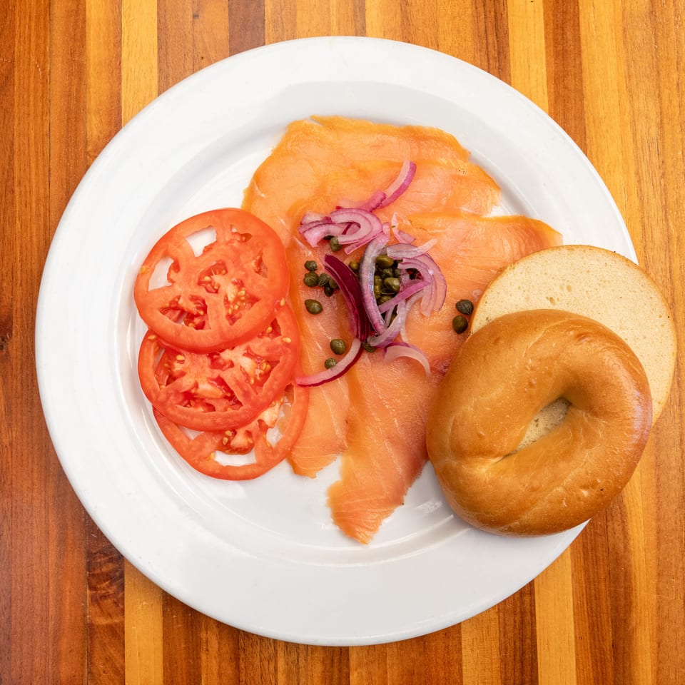 Smoked salmon with capers, red onions, tomato slices, and a bagel on a white plate.