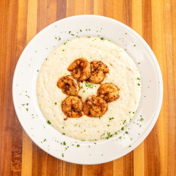A white plate of creamy grits topped with seasoned shrimp and sprinkled with parsley.
