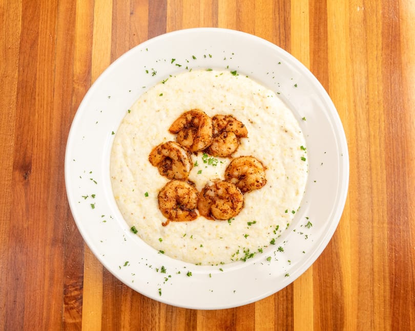 A white plate of creamy grits topped with seasoned shrimp and sprinkled with parsley.