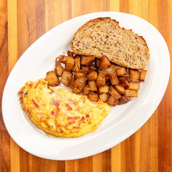 A breakfast plate with a fluffy omelet, crispy home fries, and a slice of whole wheat toast.