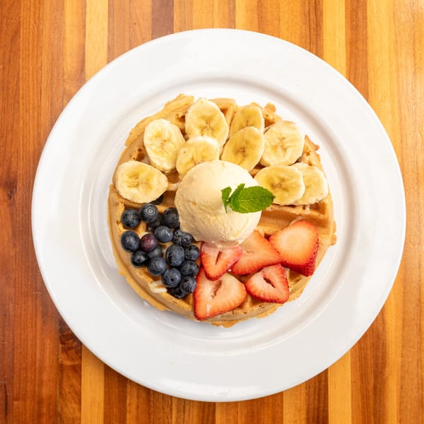 Golden waffle topped with sliced bananas, blueberries, strawberries, and a scoop of vanilla ice cream.