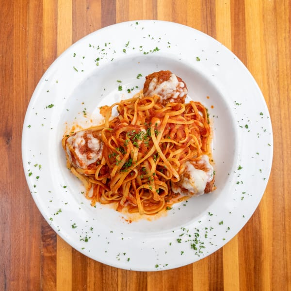 Linguine pasta with meatballs, marinara sauce, and melted cheese, garnished with parsley.
