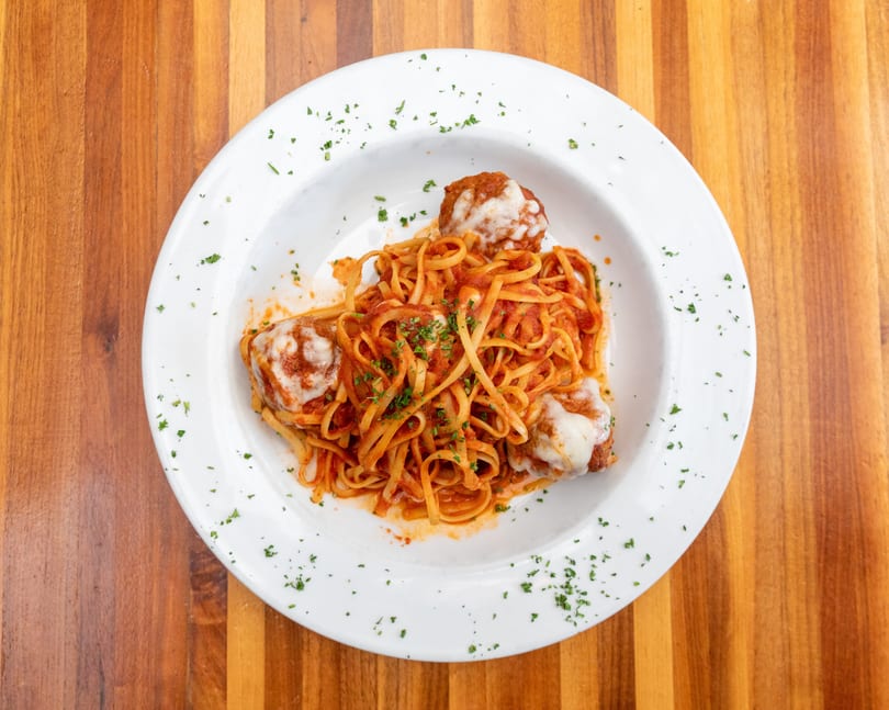 Linguine pasta with meatballs, marinara sauce, and melted cheese, garnished with parsley.